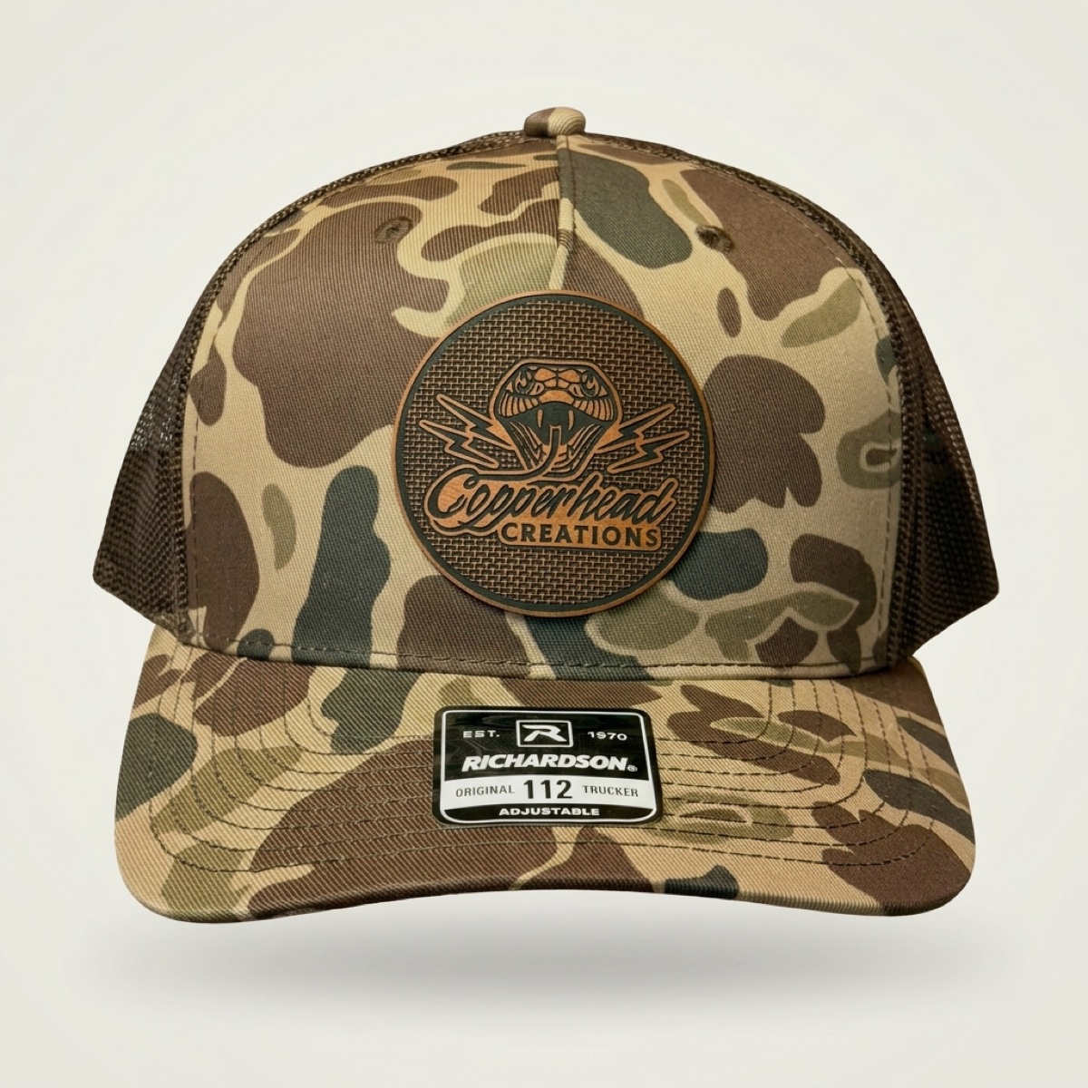 Copperhead Creations duck camo trucker cap with engraved rawhide leatherette snake logo patch