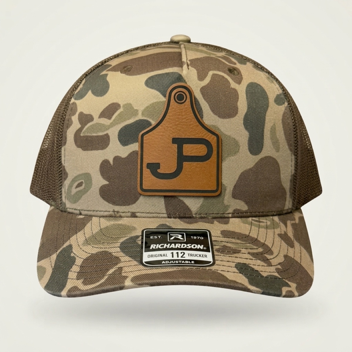 Camo Richardson trucker cap with engraved James Pugh JP cattle tag logo patch