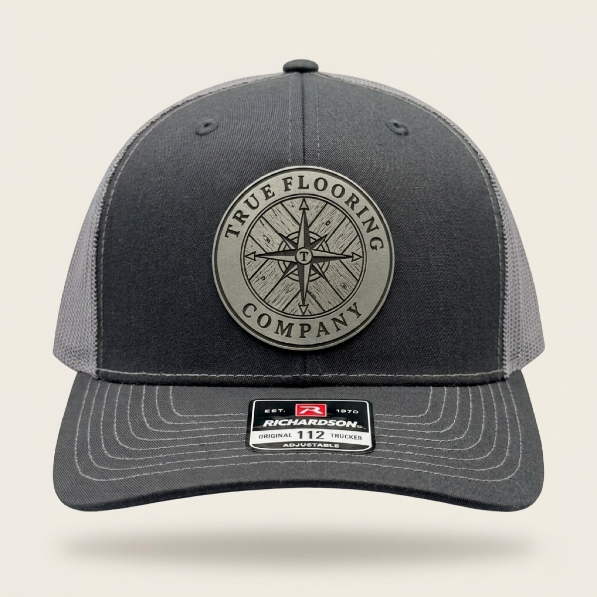 Charcoal and black Richardson trucker cap with engraved True Flooring Company compass logo patch